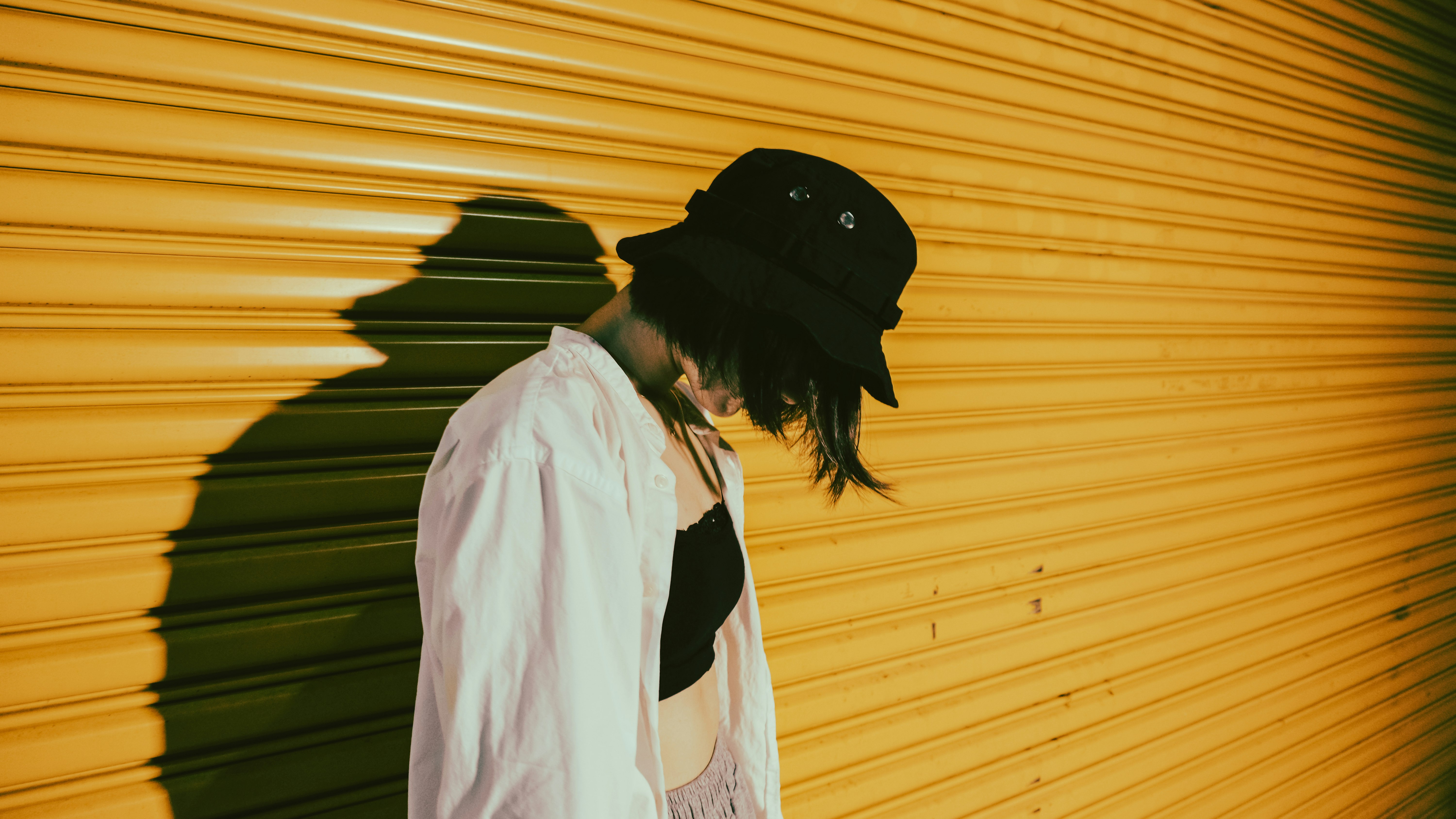 woman in white long sleeve shirt and black cap standing beside yellow wall